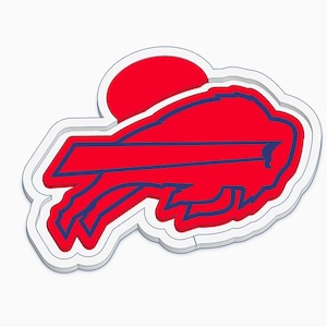 May include: A three-dimensional wall emblem featuring the Buffalo Bills logo. The design consists of a red bison silhouette with a dark blue outline, positioned in front of a red circle, all set against a raised white border and base.