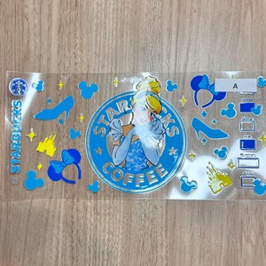 May include: A clear decal sheet featuring a central blue circular logo with a character illustration and the text STARBUCKS COFFEE. Surrounding elements include blue mouse ears, yellow castle silhouettes, blue glass slippers, yellow stars, and a checklist labeled A.