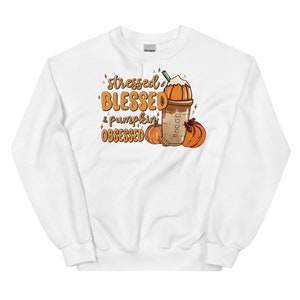 Puede incluir: Sudadera blanca con el texto "stressed BLESSED & pumpkin OBSESSED" en naranja y marrón. El diseño incluye un café con leche de calabaza y calabazas. Prenda de vestir otoñal.