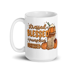 以下が含まれることがあります： 「stressed, blessed, & pumpkin obsessed」のオレンジ色の文字が入った白いセラミックマグ。マグカップは、パンプキン スパイス ラテとカボチャを使った秋をテーマにしたデザインです。
