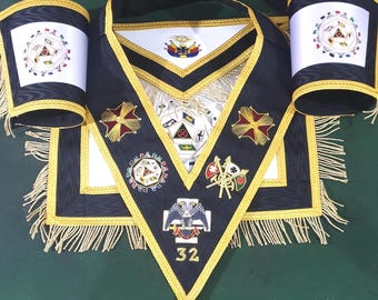 Op de afbeelding: Een set vrijmetselaarsregalia, waaronder een zwarte schort, kraag en armbanden. De schort en kraag zijn voorzien van gouden randen, geborduurde symbolen en het nummer 32. De armbanden hebben een witte achtergrond met kleurrijke emblemen en gouden franjes.