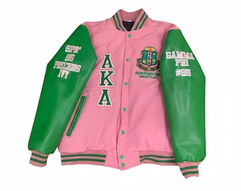 Op de afbeelding: Roze en groene varsity jas met de letters "AKA" op de voorkant. De jas heeft groene mouwen met de tekst "SPR '95 PRECIOUS IVY" en "GAMMA PHI #95". Een wapen staat op de borst.