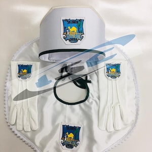 Op de afbeelding: Een witte ceremoniële set met een hoed, cape en handschoenen. Elk stuk heeft een wapen met een kameel en de woorden "SOLOMON SHEBA". De cape heeft een groene rand en de handschoenen zijn wit.