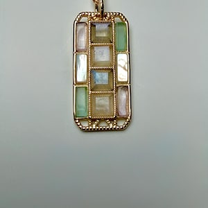 May include: A gold-toned pendant necklace with a rectangular pendant. The pendant features a grid of rectangular and square-shaped sections in pastel colors, including pink, green, and white. The necklace has a delicate chain.