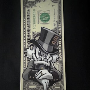May include: A one-dollar bill featuring a cartoon illustration of a duck wearing a top hat and a suit. The duck is depicted with a stern expression, and the bill's details are visible, including the serial number and the words "ONE DOLLAR".