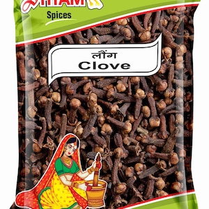Puede incluir: Un paquete verde y rojo de Shyam Spices lleno de clavos de olor marrones. El paquete tiene texto en inglés e hindi, y un gráfico de una mujer moliendo especias. Peso neto: 50g.