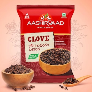 Puede incluir: Una bolsa roja de especias enteras Aashirvaad, con la palabra "CLOVE" en un lugar destacado. La imagen muestra cuencos de madera y una cuchara llenos de clavos, lo que ilustra el producto. El embalaje destaca las cualidades "PURE & NATURAL".