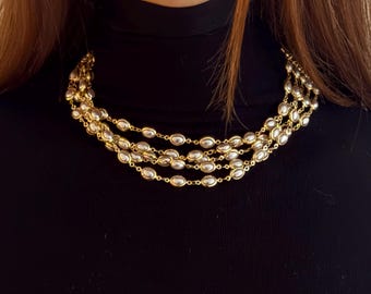 May include: A multi-strand necklace featuring oval-shaped, silver-toned beads encased in gold-colored metal. The necklace is layered, creating a cascading effect. The jewelry is worn against a black turtleneck.