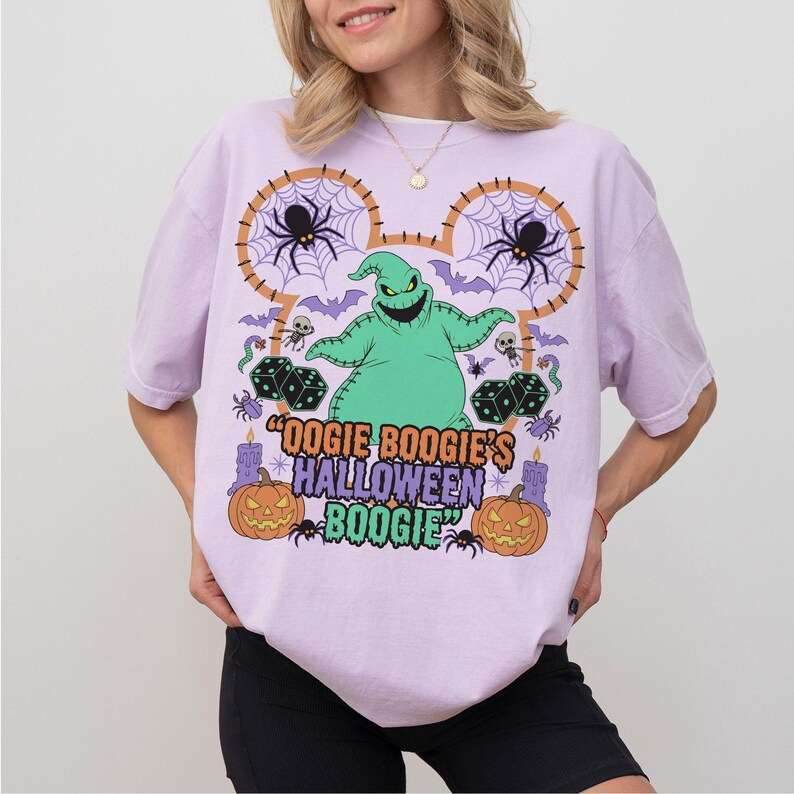 May include: A light purple t-shirt featuring a graphic of Oogie Boogie from The Nightmare Before Christmas. The design includes spiders, bats, dice, pumpkins, and the text "Oogie Boogie's Halloween Boogie".
