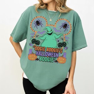 May include: A green t-shirt featuring a graphic of Oogie Boogie from The Nightmare Before Christmas. The design includes spiders, dice, bats, pumpkins, and the text "Oogie Boogie's Halloween Boogie".