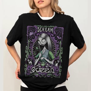 K&ouml;nnte beinhalten: Schwarzes T-Shirt mit einer Grafik einer Figur mit langen wei&szlig;en Haaren, die ein gr&uuml;nes Kleid tr&auml;gt, und dem Text "SCREAM QUEEN" in einem lila Rahmen mit Spinnweben und Flederm&auml;usen. Das T-Shirt hat einen wei&szlig;en Kragen.