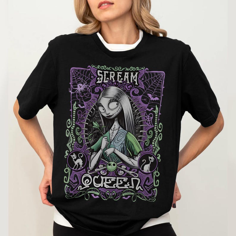K&ouml;nnte beinhalten: Schwarzes T-Shirt mit einer Grafik einer Figur mit langen wei&szlig;en Haaren, die ein gr&uuml;nes Kleid tr&auml;gt, und dem Text "SCREAM QUEEN" in einem lila Rahmen mit Spinnweben und Flederm&auml;usen. Das T-Shirt hat einen wei&szlig;en Kragen.