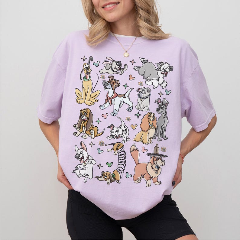 May include: A light purple t-shirt featuring a collection of cartoon dog illustrations. The dogs are in various poses and colors, with some wearing hats or accessories. The shirt has a relaxed fit.