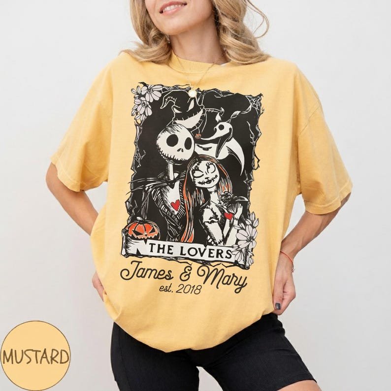 May include: Mustard-colored t-shirt featuring a black and white graphic of Jack Skellington and Sally from The Nightmare Before Christmas. The graphic includes the text "THE LOVERS" and "James & Mary est. 2018".