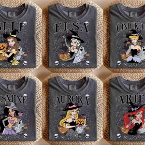 May include: Six charcoal grey t-shirts featuring Disney princesses dressed as witches for Halloween. Each shirt displays a character name, a princess in a witch hat, a pumpkin, ghosts, and skulls. The designs include Belle, Elsa, Cinderella, Jasmine, Aurora, and Ariel.