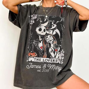 May include: Dark gray t-shirt featuring a graphic of Jack Skellington and Sally from The Nightmare Before Christmas. The design includes the words "THE LOVERS" and "James & Mary est. 2018". The shirt has a vintage, worn look.