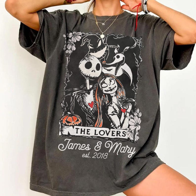 May include: Dark gray t-shirt featuring a graphic of Jack Skellington and Sally from The Nightmare Before Christmas. The design includes the words "THE LOVERS" and "James & Mary est. 2018". The shirt has a vintage, worn look.