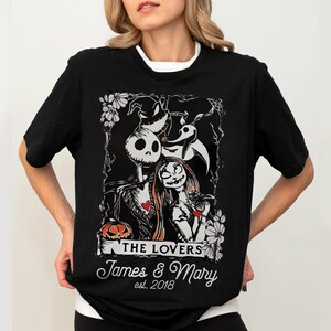 May include: Black t-shirt featuring a graphic of Jack Skellington and Sally from The Nightmare Before Christmas, with the text "THE LOVERS" and personalized names "James & Mary" and the year "est. 2018".