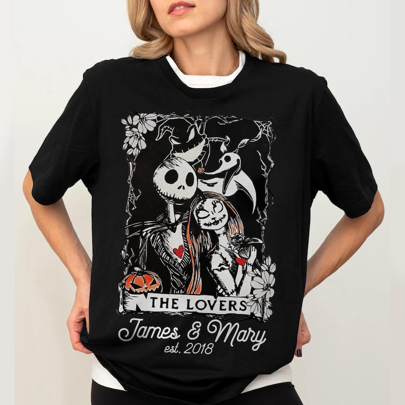 May include: Black t-shirt featuring a graphic of Jack Skellington and Sally from The Nightmare Before Christmas, with the text "THE LOVERS" and personalized names "James & Mary" and the year "est. 2018".