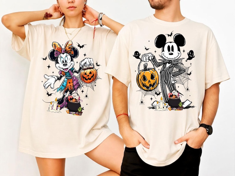 May include: Beige t-shirts featuring Halloween-themed cartoon characters. One shirt displays Minnie Mouse in a witch costume holding a jack-o'-lantern. The other shirt shows Mickey Mouse dressed as Jack Skellington, also with a pumpkin.