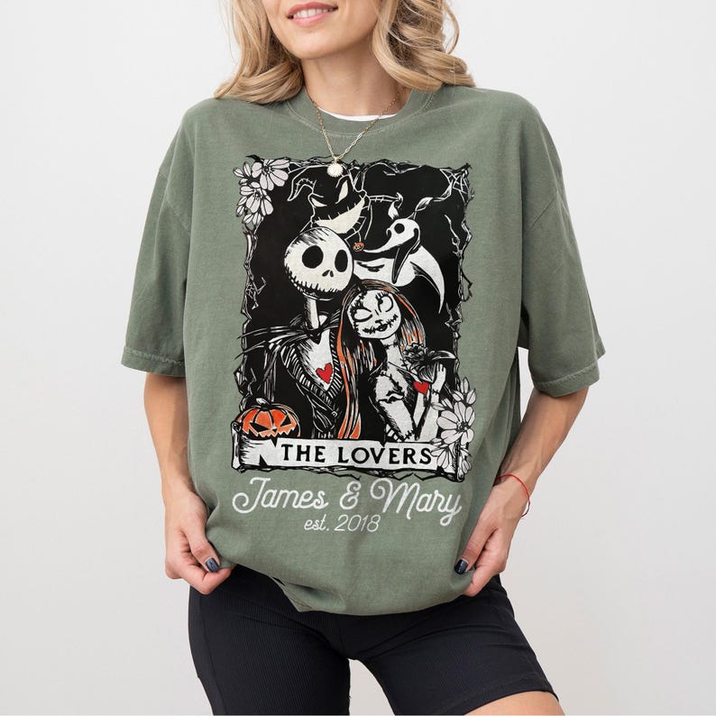May include: Sage green t-shirt featuring a black and white graphic of Jack and Sally from The Nightmare Before Christmas. The graphic includes the text "THE LOVERS" and "James & Mary est. 2018".