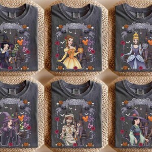 May include: Six charcoal grey t-shirts featuring various animated characters in Halloween costumes. Each shirt displays a unique character, including a witch, a princess, and a mummy, surrounded by pumpkins, spiderwebs, and castle silhouettes.