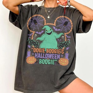 May include: Dark gray t-shirt featuring a colorful graphic of Oogie Boogie from The Nightmare Before Christmas. The design includes spiders, dice, pumpkins, and the text "Oogie Boogie's Halloween Boogie".