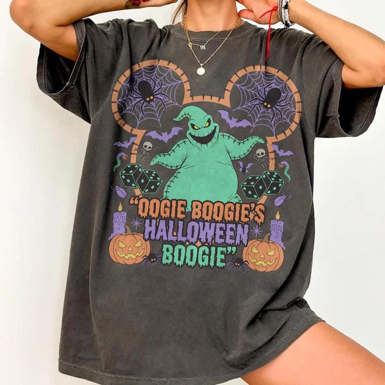 May include: Dark gray t-shirt featuring a colorful graphic of Oogie Boogie from The Nightmare Before Christmas. The design includes spiders, dice, pumpkins, and the text "Oogie Boogie's Halloween Boogie".