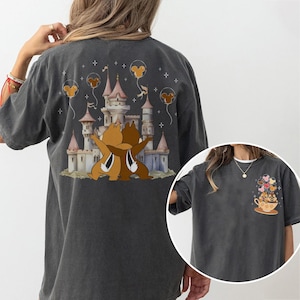 May include: Dark gray t-shirt featuring a whimsical illustration of a castle with Chip and Dale embracing. The design includes Mickey Mouse-shaped balloons and stars. A smaller image on the right shows Chip and Dale in a teacup with heart-shaped balloons.