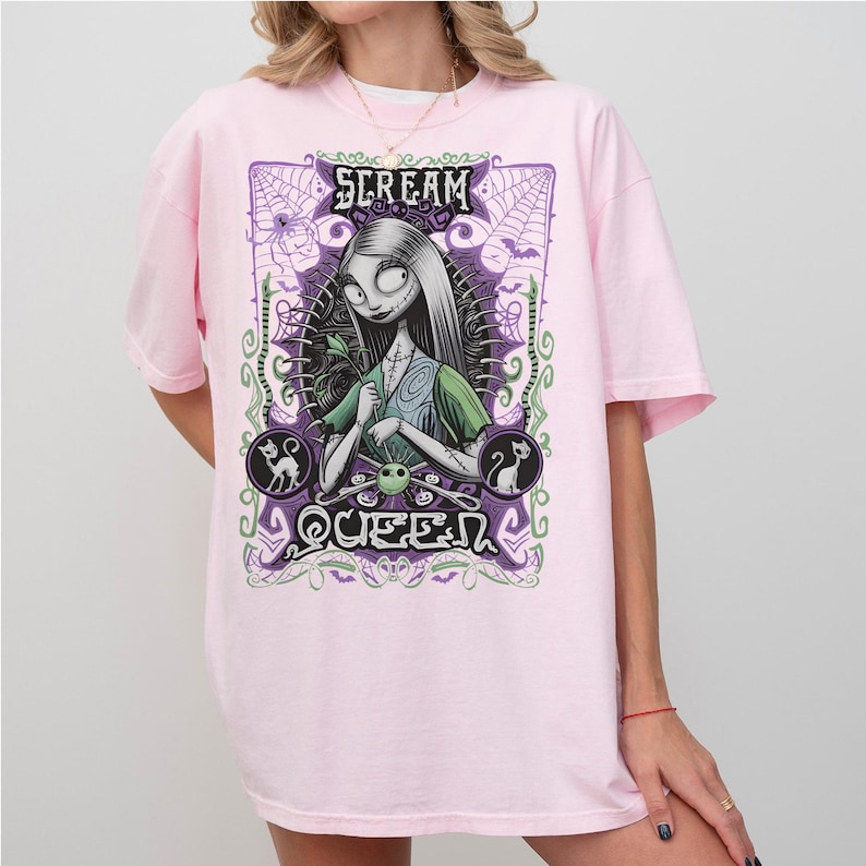 K&ouml;nnte beinhalten: Hellrosa T-Shirt mit einem Aufdruck von Sally aus The Nightmare Before Christmas. Das Design enth&auml;lt den Text "SCREAM QUEEN", Spinnweben und andere Halloween-Elemente in Lila und Gr&uuml;n.