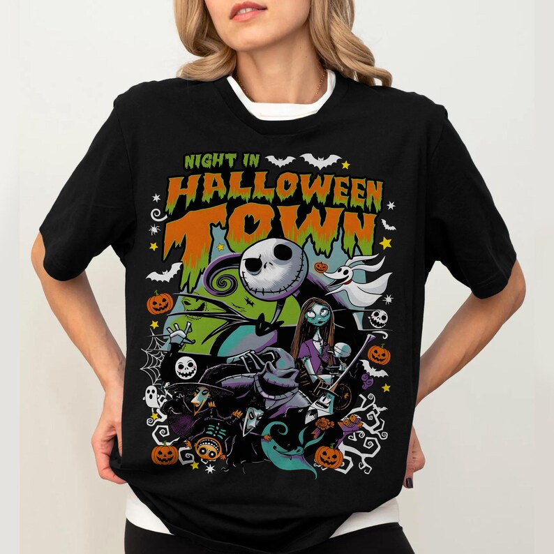 May include: Black t-shirt featuring a colorful graphic from "The Nightmare Before Christmas." The design includes Jack Skellington, Sally, Zero, and other characters, with the text "Night in Halloween Town."