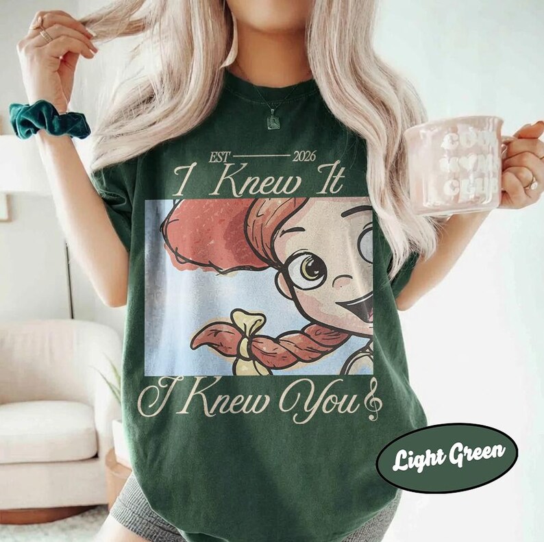May include: A dark green short-sleeve t-shirt featuring a graphic of a cartoon character with red hair in a ponytail. The text reads EST 2026 I Knew It I Knew You. The shirt has a crew neckline and a relaxed fit, showcasing a vintage-inspired design.
