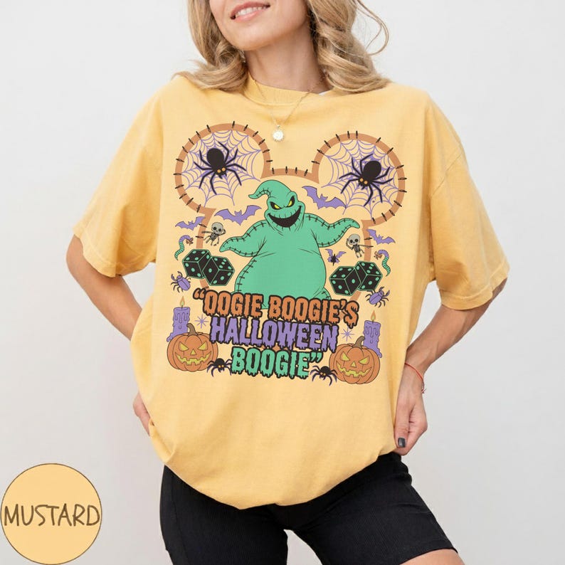 May include: Mustard-colored t-shirt featuring a green Oogie Boogie character design with the text "Oogie Boogie's Halloween Boogie". The design includes spiders, dice, bats, and pumpkins, perfect for Halloween.