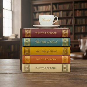 May include: A stack of five books with gold lettering and decorative accents. Each book has a different color spine: burgundy, teal, yellow, orange, and cream. A white teacup and saucer with the name "Carol" in gold lettering sits atop the books.