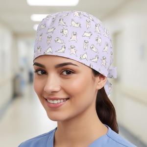 May include: A light purple surgical scrub cap featuring a repeating pattern of cartoon pugs in various yoga poses. The cap has a tie in the back and is made of a soft, lightweight fabric. The background is a blurred hospital hallway.