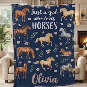 Puede incluir: Manta azul marino con ilustraciones de caballos, flores rosas y hojas verdes. La manta tiene el texto "Just a girl who loves HORSES" y el nombre "Olivia" en cursiva.