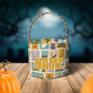 Könnte beinhalten: Ein zylindrischer Stoffeimer mit Henkel, der mit einem wiederkehrenden Muster aus bunten, briefmarkenartigen Illustrationen von Halloween-Motiven wie Kürbissen, Geistern, Skeletten und Fledermäusen bedruckt ist, mit dem Wort NAME in großen Goldbuchstaben.