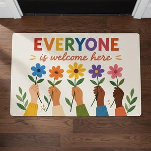 May include: A rectangular welcome mat with the words "EVERYONE is welcome here" in colorful letters. The mat features illustrations of hands holding flowers in various colors, including blue, orange, yellow, purple, and pink.