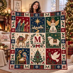 Könnte beinhalten: Eine gesteppte Weihnachtsdecke mit neun Feldern, die die Geburt Christi, ein Kamel, ein Schaf, einen Engel, einen Weihnachtsbaum, eine Taube und ein zentrales Monogramm mit dem Buchstaben M und dem Text THE MILLERS zeigen, umrandet von einem Karomuster.