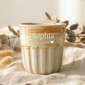 Könnte beinhalten: Becher aus Keramik in Creme- und Brauntönen mit geripptem Design. Der Becher trägt den Namen "Sophia" und das Jahr "EST.2026" mit einem Herzsymbol. Geeignet für Heiß- oder Kaltgetränke.