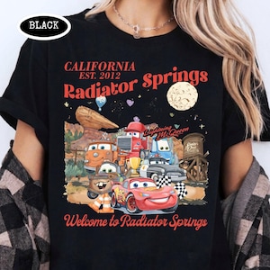 May include: Black t-shirt featuring a colorful graphic of characters from the movie Cars, with the text "California Radiator Springs" and "Welcome to Radiator Springs". The design includes a moon, desert landscape, and the text "Lightning McQueen".