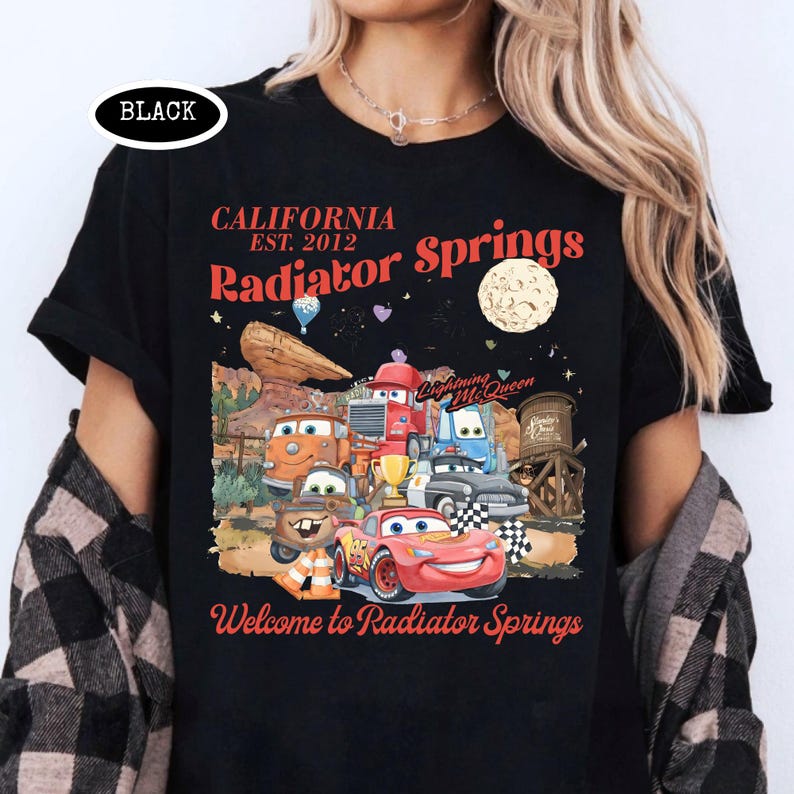 May include: Black t-shirt featuring a colorful graphic of characters from the movie Cars, with the text "California Radiator Springs" and "Welcome to Radiator Springs". The design includes a moon, desert landscape, and the text "Lightning McQueen".