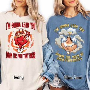 May include: Two long-sleeved shirts, one ivory and one blue jean, each with a graphic and text. The ivory shirt features a red devil graphic with the text "I'M GONNA LEAD YOU DOWN THE PATH THAT ROCKS." The blue jean shirt has an angel graphic with the text "I'M GONNA LEAD YOU DOWN THE PATH OF RIGHTEOUSNESS."
