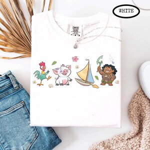 May include: White t-shirt featuring cartoon characters. The design includes a rooster, a pig, a sailboat, and a character holding a weapon. The word "WHITE" is in a black oval at the top. The shirt is a Comfort Colors brand.