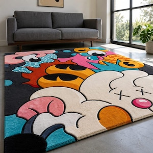 May include: A colorful area rug with a cartoon-style design. The rug features a black background with large, abstract shapes in white, pink, orange, yellow, and blue. The rug is placed on a gray floor.