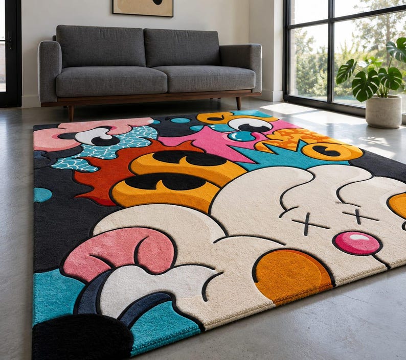 May include: A colorful area rug with a cartoon-style design. The rug features a black background with large, abstract shapes in white, pink, orange, yellow, and blue. The rug is placed on a gray floor.