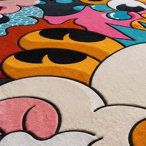 May include: A colorful, abstract rug with a playful design. The rug features a variety of shapes and colors, including orange, yellow, pink, blue, and white. The design has a cartoonish, pop art style.