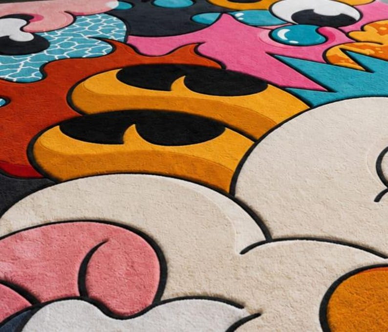 May include: A colorful, abstract rug with a playful design. The rug features a variety of shapes and colors, including orange, yellow, pink, blue, and white. The design has a cartoonish, pop art style.