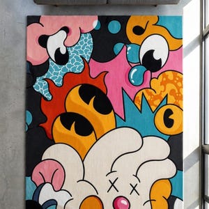 May include: A rectangular rug with a colorful, cartoonish design. The rug features a black background with various shapes in pink, orange, blue, and white. A gray sofa is visible above the rug.