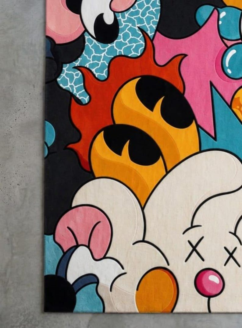 May include: A colorful, abstract rug with a cartoonish design. The rug features a variety of shapes and colors, including black, orange, pink, blue, and white. The design includes flame-like shapes, a cloud-like figure with crossed-out eyes, and other playful elements.